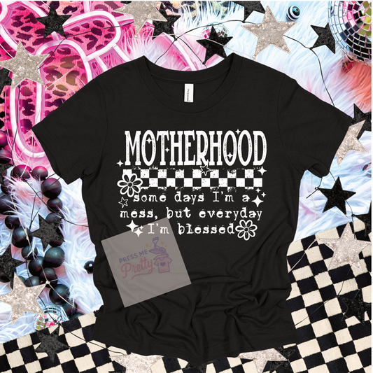 Black t-shirt with 'Motherhood' text design on a decorative background